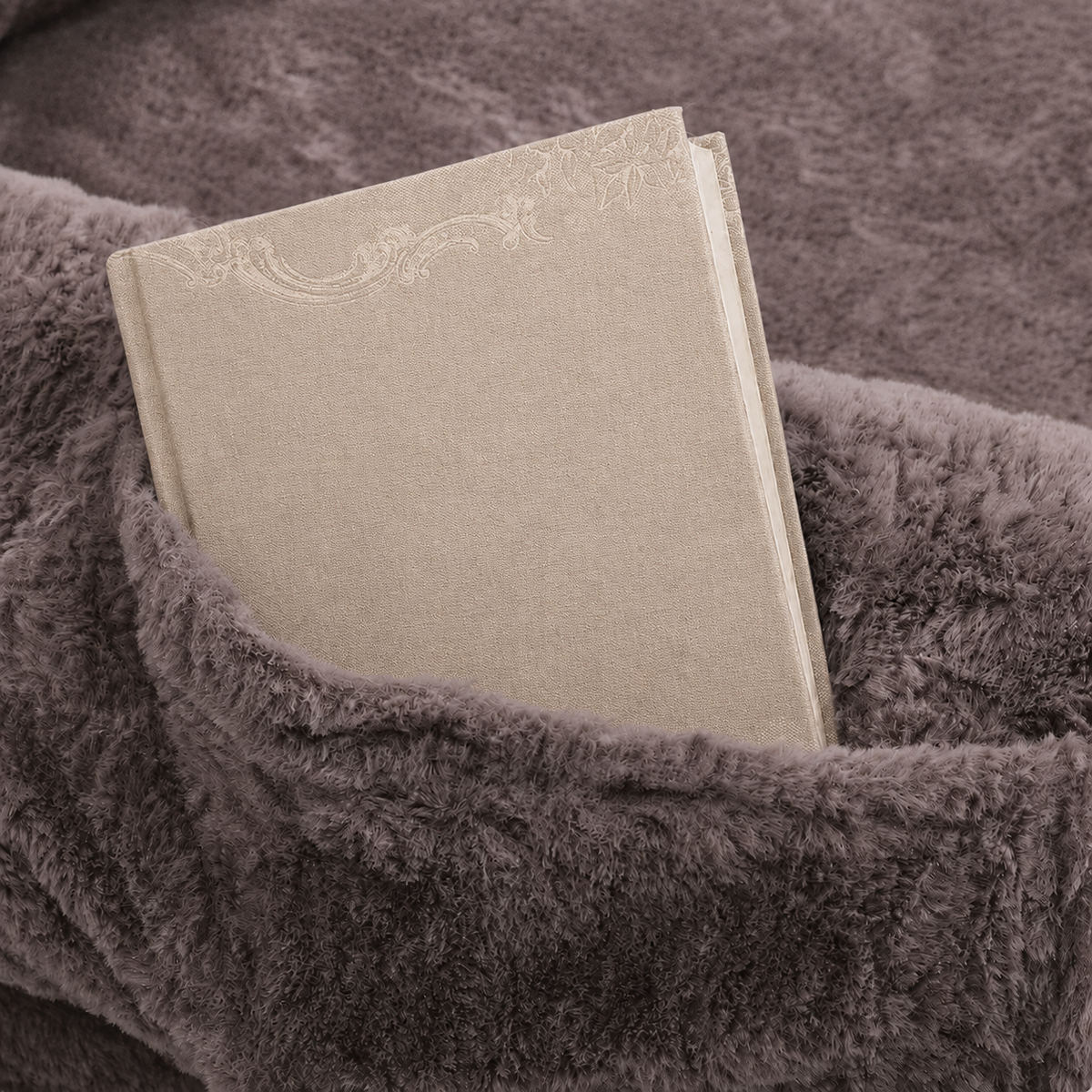 A beige fabric-covered book or notebook with a subtle embossed floral design, tucked into a plush, textured gray blanket.
